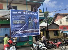 Bhabinkamtibmas Ritabel dibantu personil Polsek Larat pasang Spanduk New Normal di khalayak ramai sekaligus laksanakan Sosialisasi